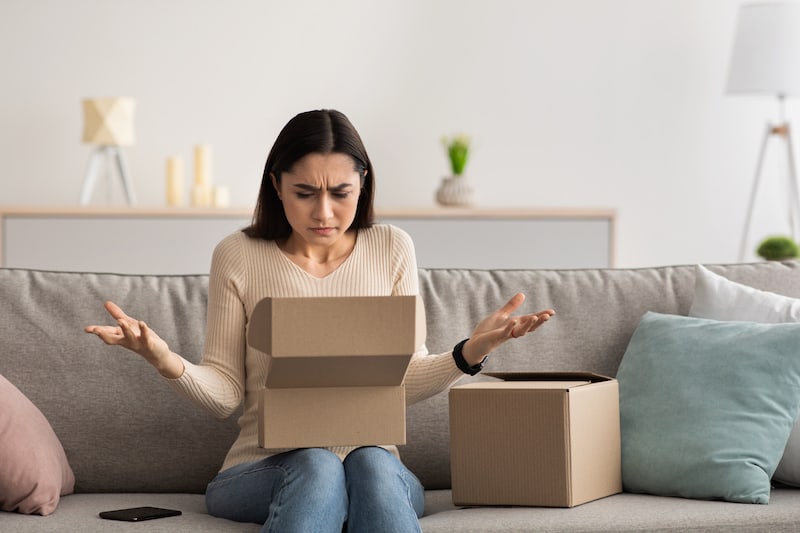 Upset woman looking at a box on her lap upset about delivery issues
