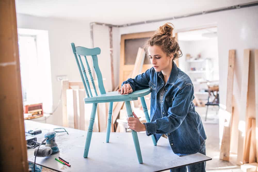 young woman sanding a chair restoration furniture company concept