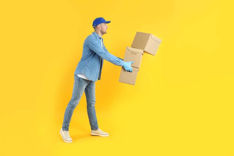 Delivery man holding parcel boxes with one falling portraying shipping insurance concept